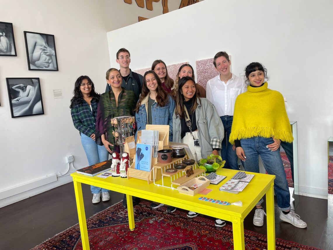 a group of students standing in front of a yellow table with zines and artwork.