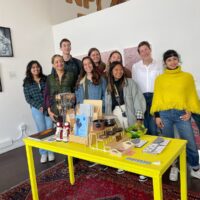 a group of students standing in front of a yellow table with zines and artwork.