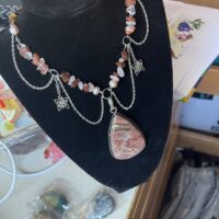 A work in progress with a silver necklace in the process of being recycled. Pliers and wires lie around the desk workspace.