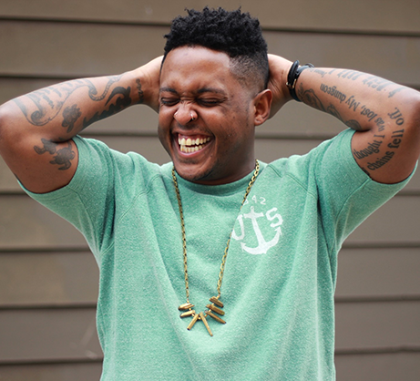 Photo of Danez Smith in a mint green t shirt, smiling with their hands behind their head