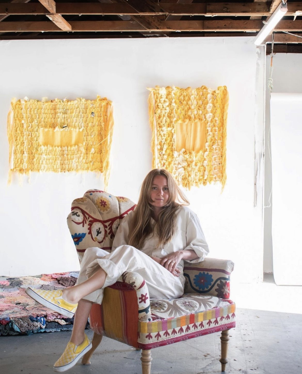 a photo of a woman with long blonde hair sitting at an angle in a brightly patterned armchair