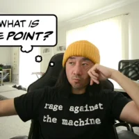 Ge Wang wearing a “Rage Against the Machine” t-shirt sits and looks to the side; a thought-bubble next to him reads, “What is the point?”