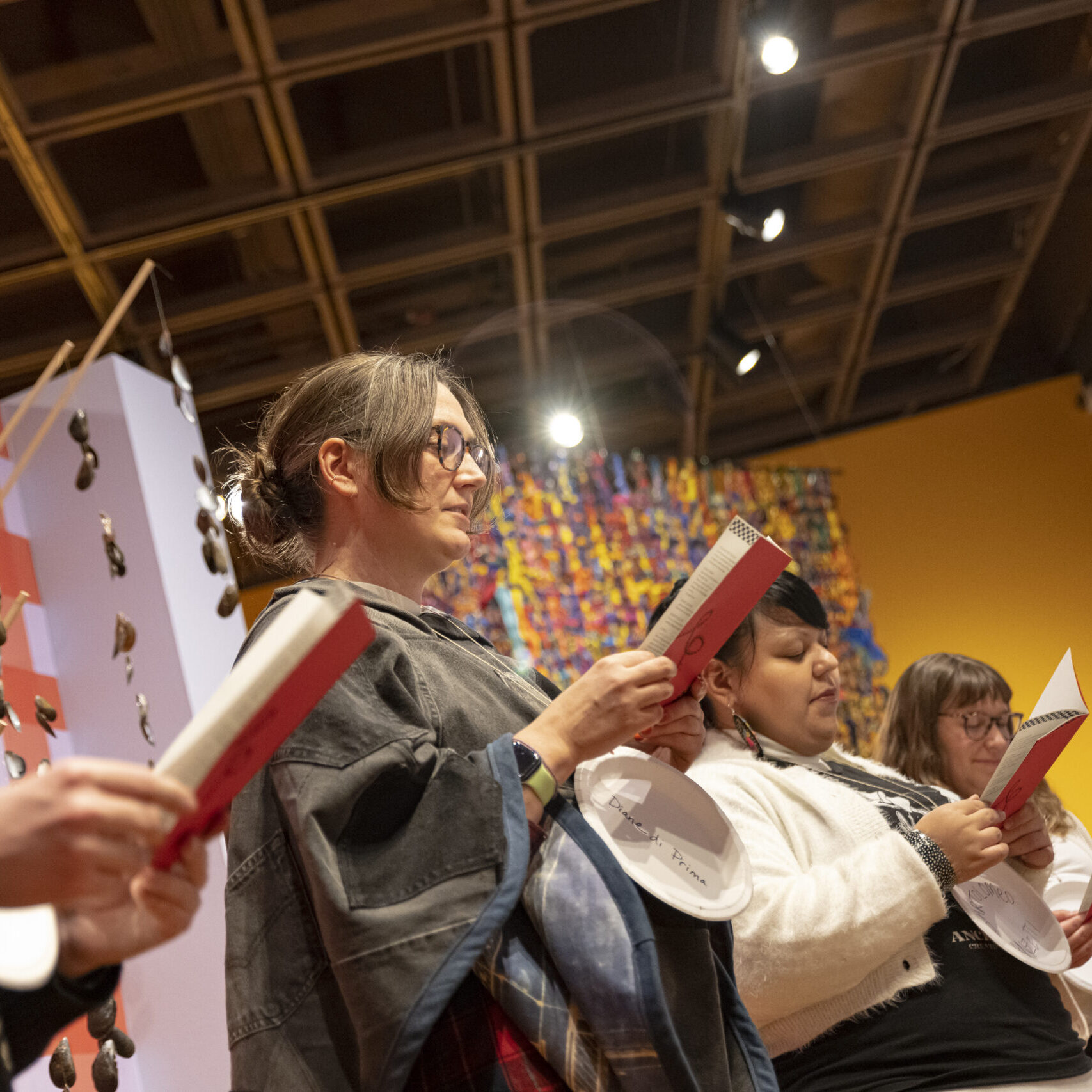 students stand reading a script in front of woven objects hanging around a gallery