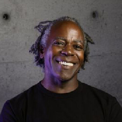 Arnold J. Kemp wearing a black t-shirt infront of a gray concrete background