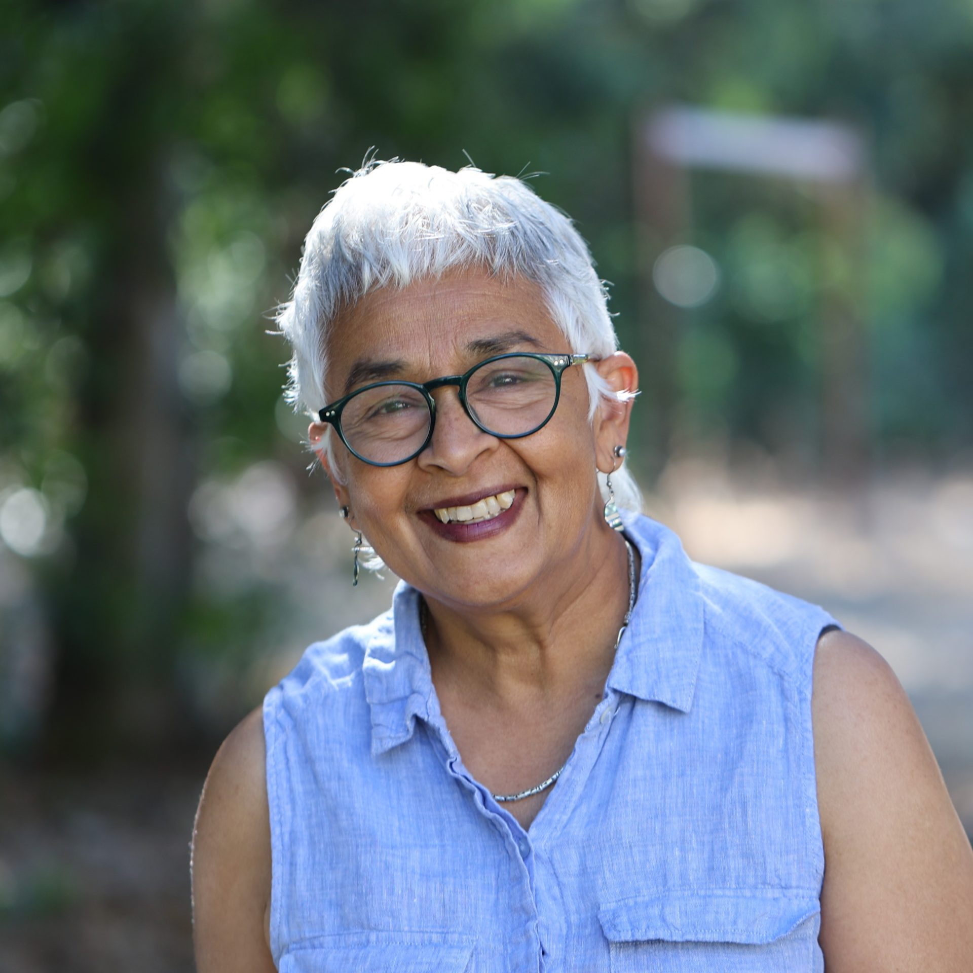 A photo of Devaki Bhaya in a lilac top in front of trees