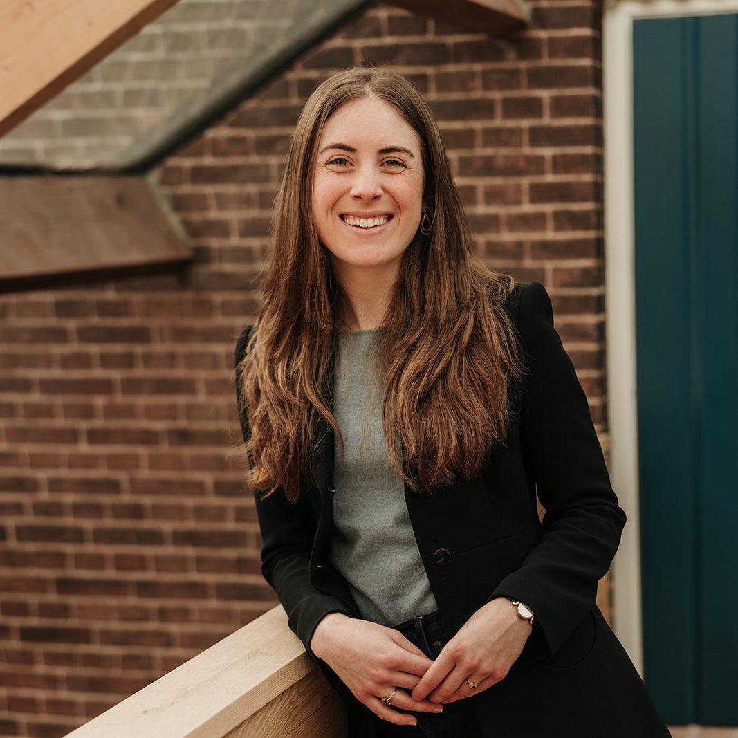 A person with long hair leaning on a railing and smiling at the camera