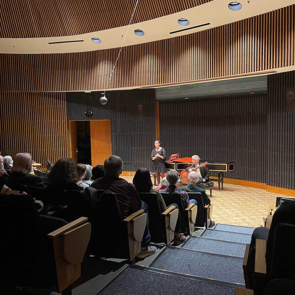 a vocalist stands in front of piano in a performance hall