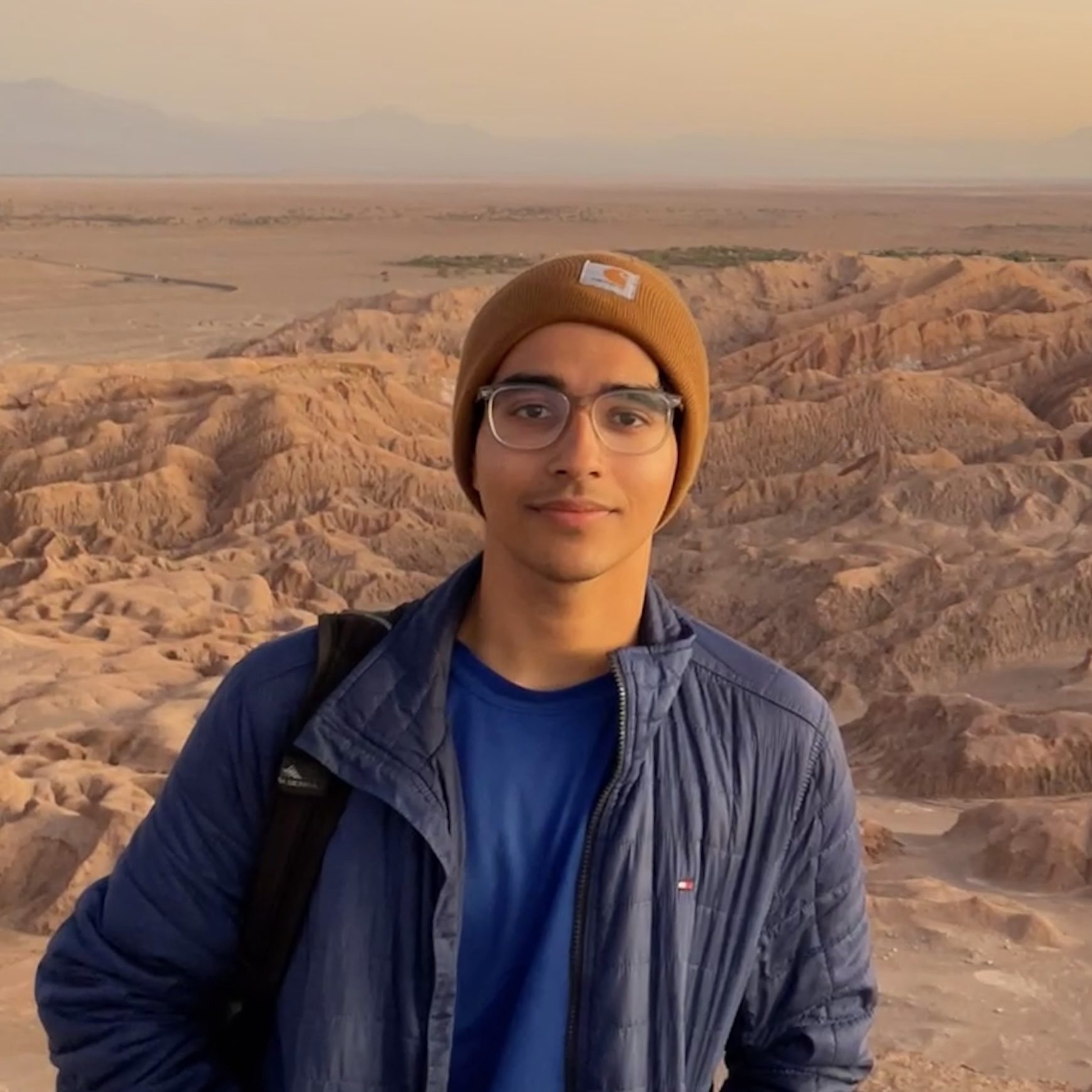Photo of Shridhar Athinarayanan wearing a blue jacket and yellow hat with a rocky landscape in the background