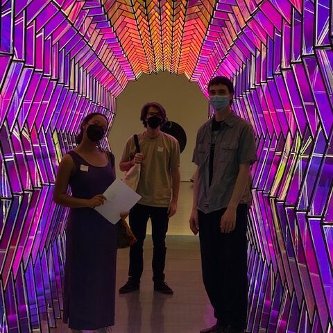 three students stand in a tunnel with purple and red hued lights