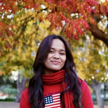 Photo of Isabella in a red sweater, with a red scarf, against the red leaves of a tree