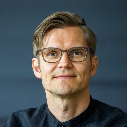 Person with glasses wearing a dark shirt staring straight into the camera.
