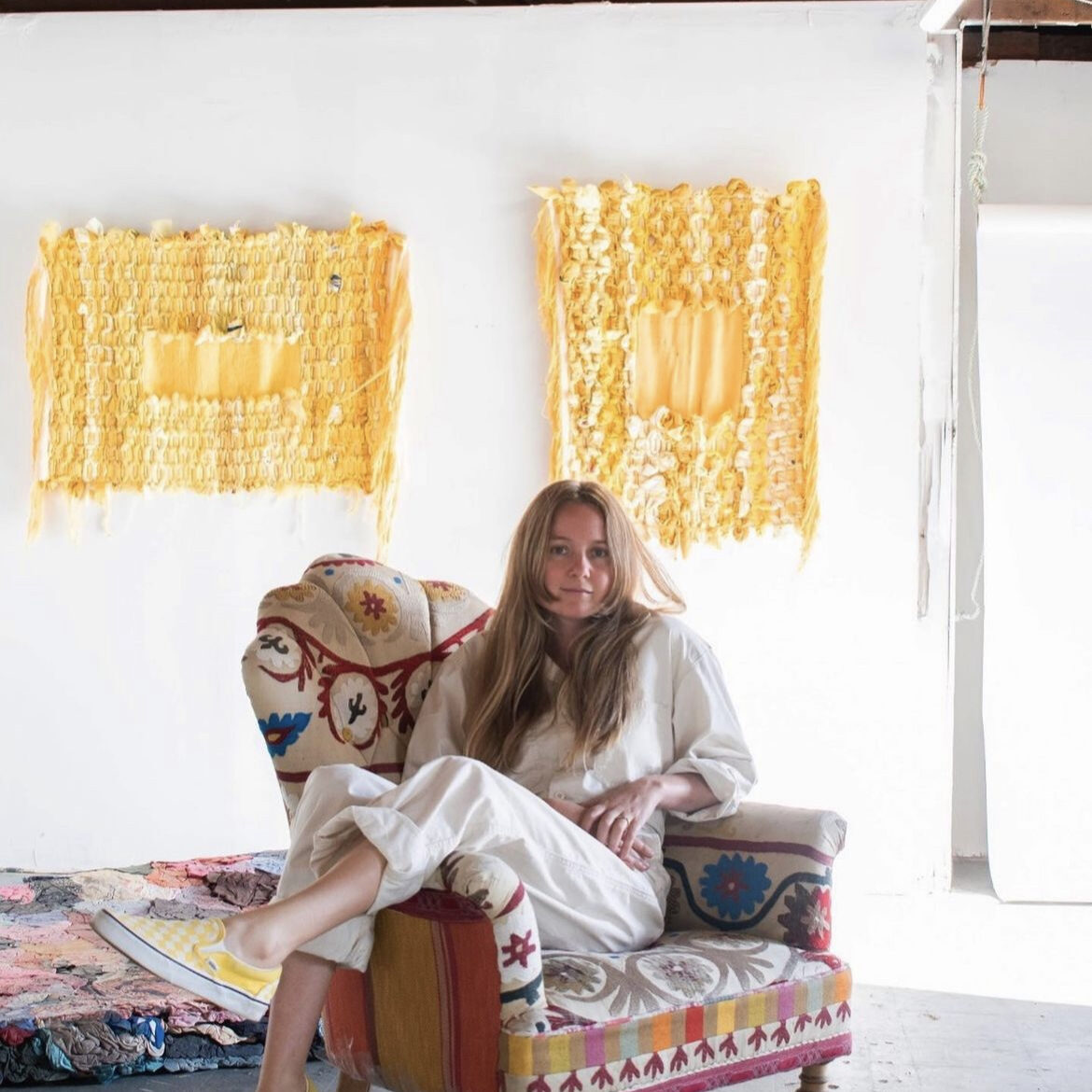 a photo of a woman with long blonde hair sitting at an angle in a brightly patterned armchair