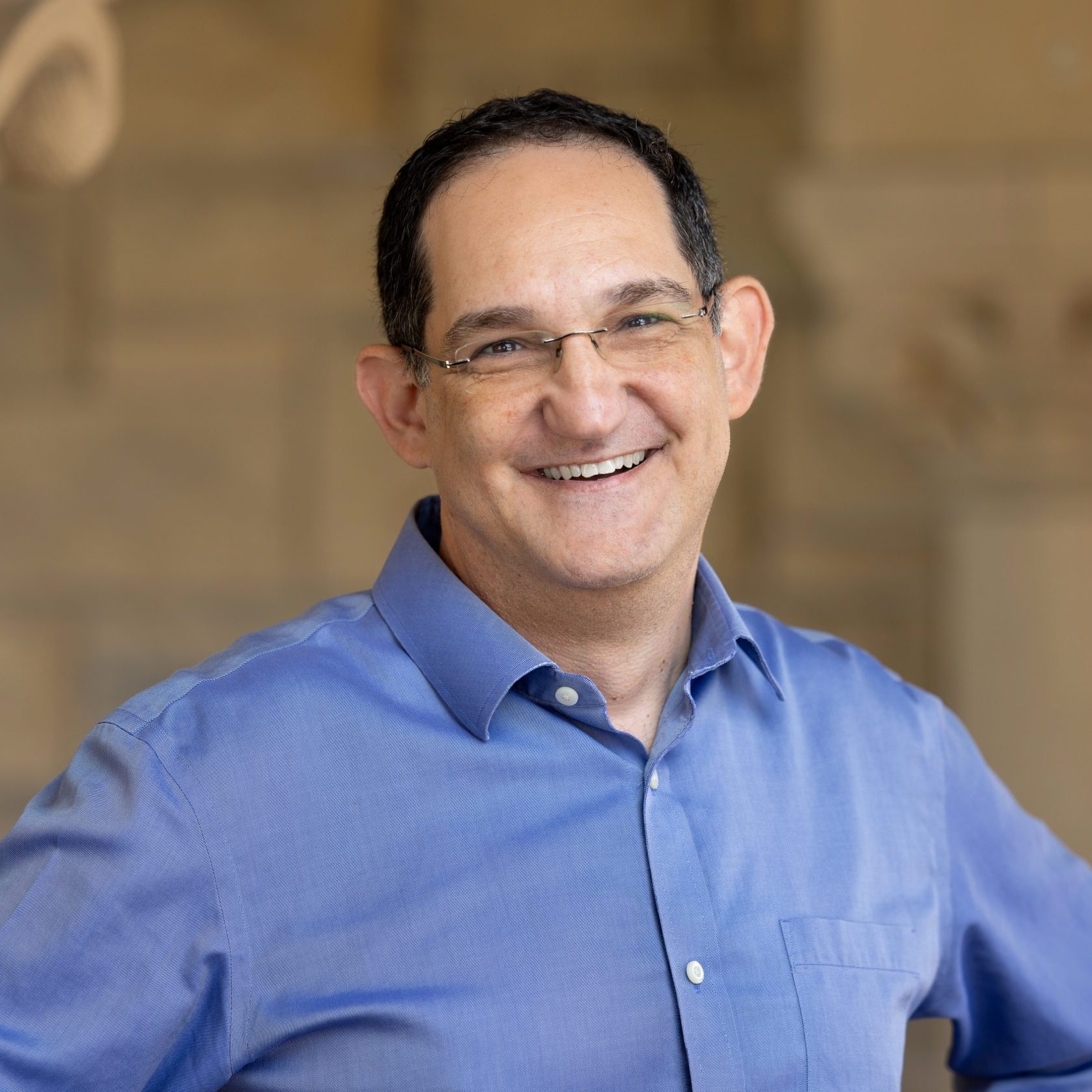 A photo of Adam Tobin, a smiling man in blue button up