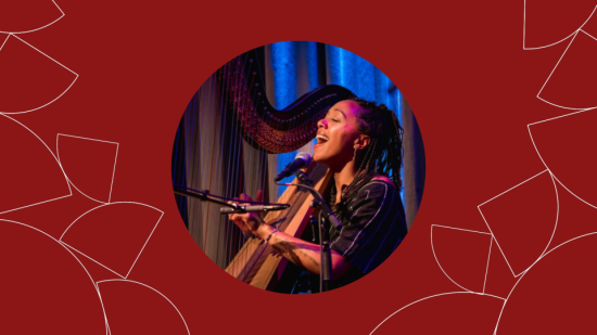Lizzie No (‘13) singing into a microphone while playing the harp onstage, lit in blue and purple.