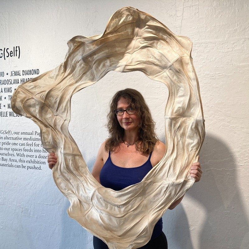 a photo of Michelle Wilson in a gallery space, holding a large circular sculpture