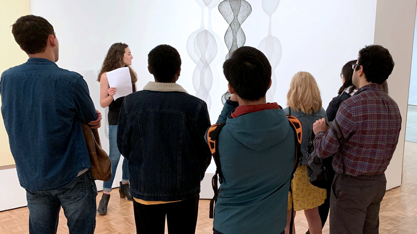 A group of students with their backs to the camera looking at a work of art.