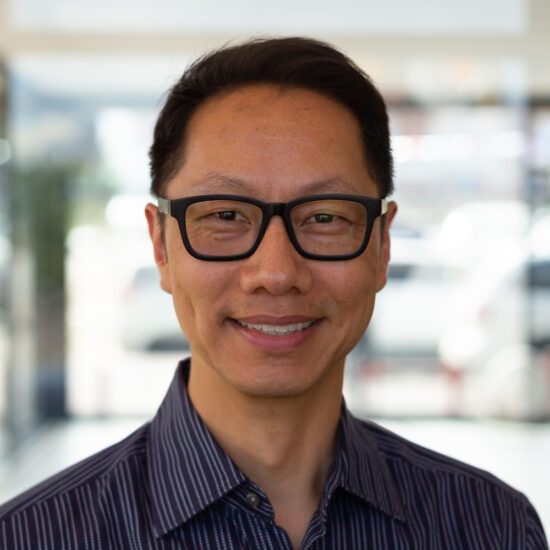 A person with glasses looking towards the camera and smiling