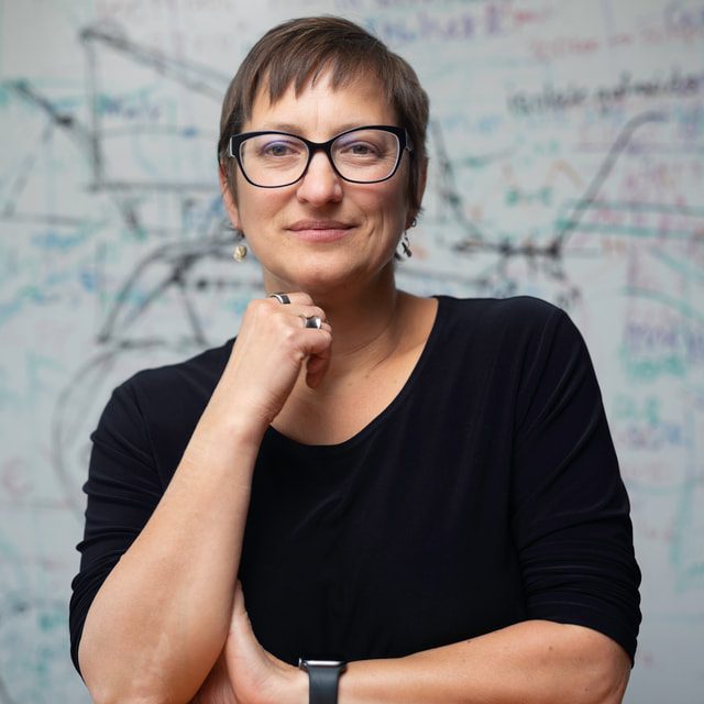 Risa Wechsler sits at a table, a white board with calculations behind her
