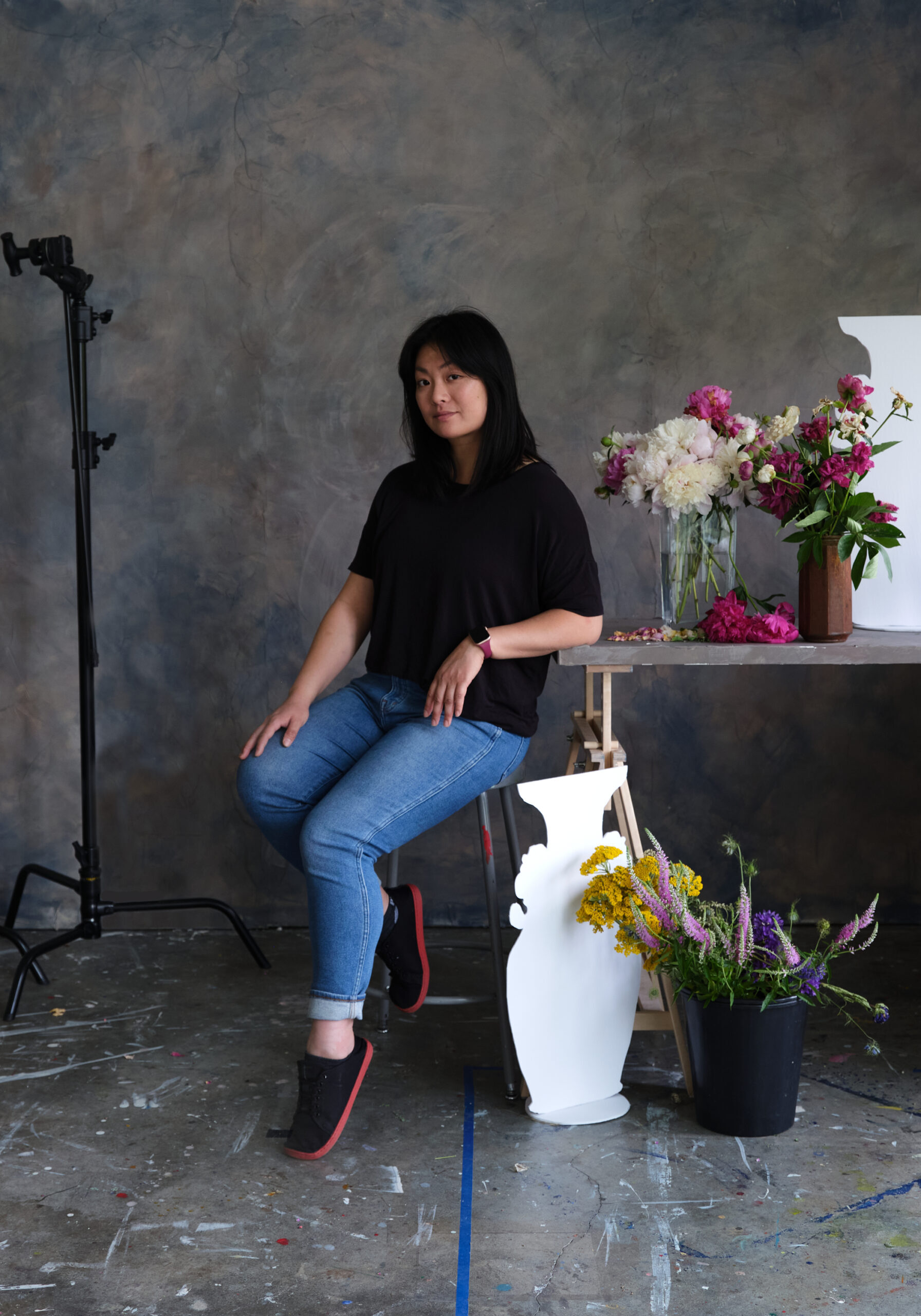 A photo of Stephanie Shih sitting next to a table with flowers and sculptures