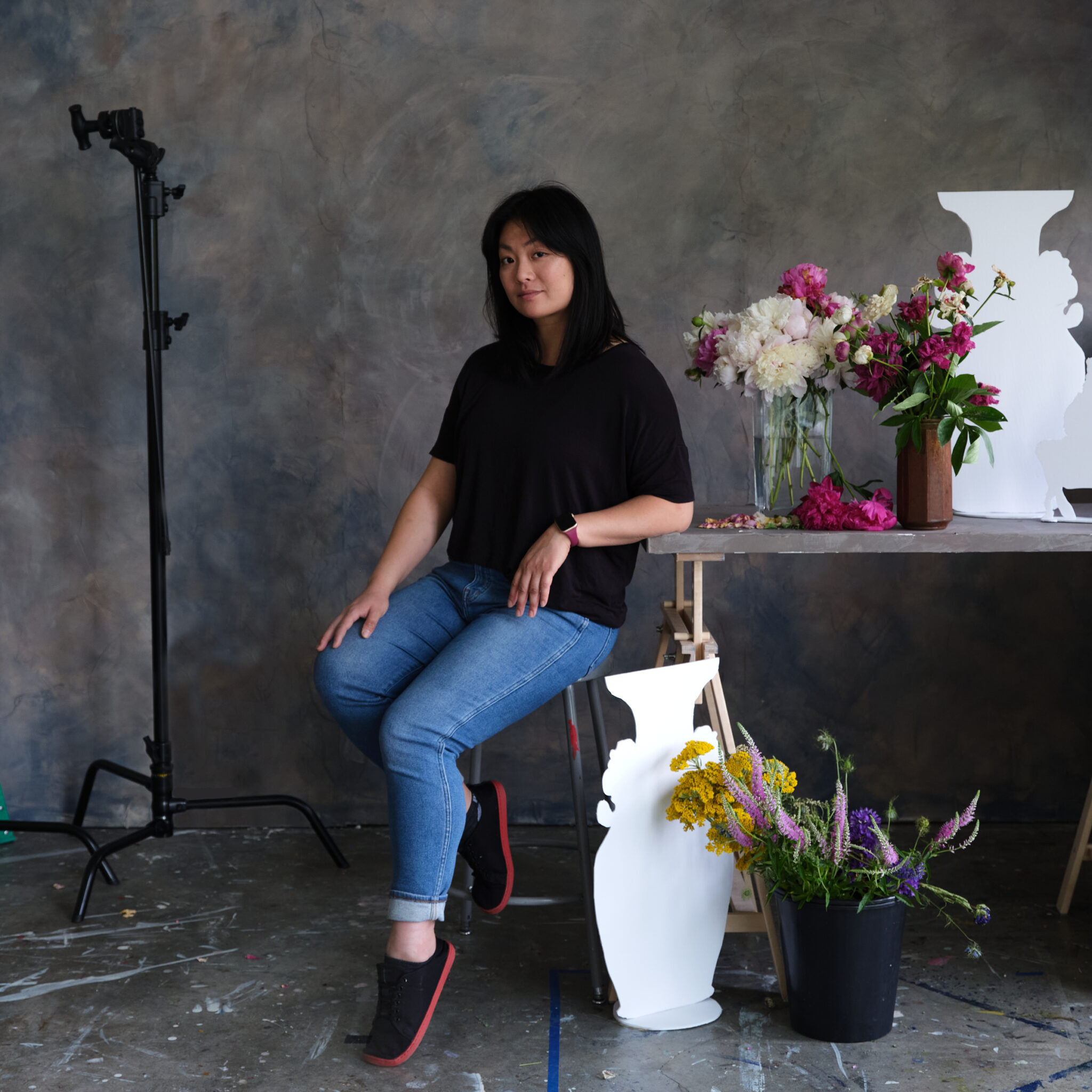 A photo of Stephanie Shih sitting next to a table with flowers and sculptures