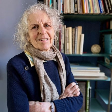 Person standing in front of a bookcase, smiling towards the camera